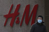 A man wearing a face mask walks by a Swedish fashion brand H&M store outlet in Beijing, March 25, 2021.
