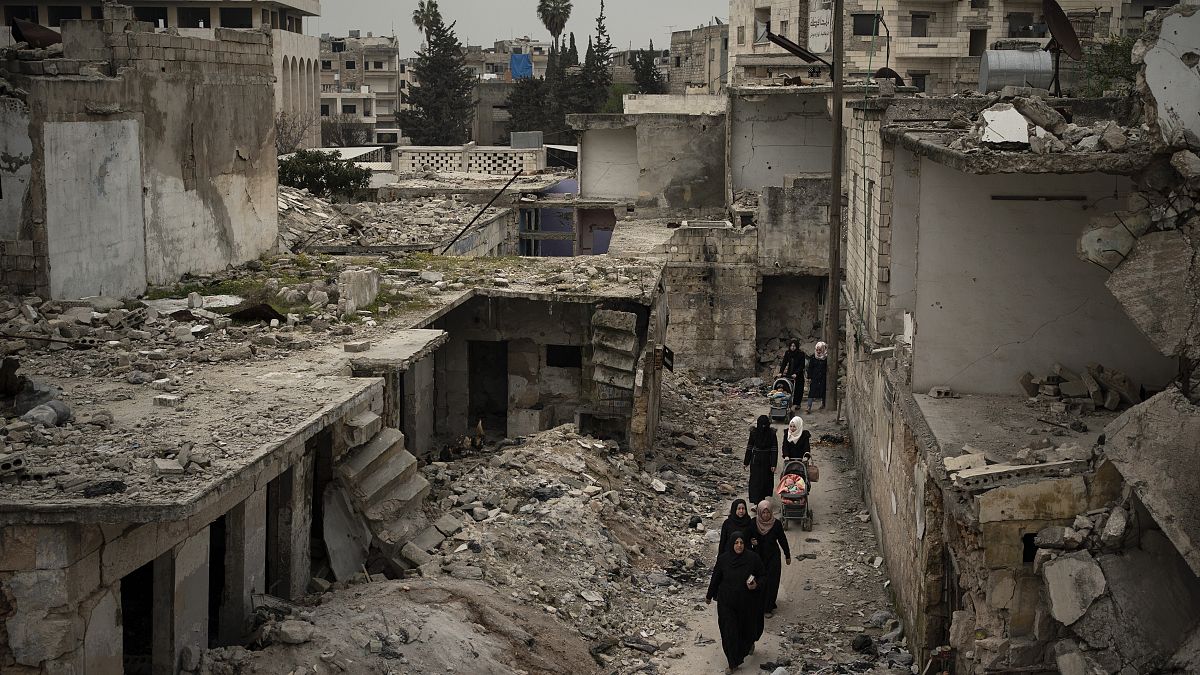 In this March 12, 2020 file photo, women walk in a neighborhood heavily damaged by airstrikes in Idlib, Syria. 