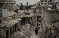 In this March 12, 2020 file photo, women walk in a neighborhood heavily damaged by airstrikes in Idlib, Syria.