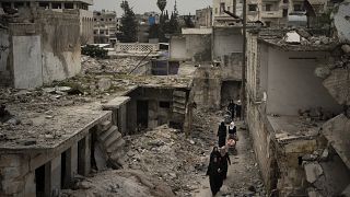 In this March 12, 2020 file photo, women walk in a neighborhood heavily damaged by airstrikes in Idlib, Syria.