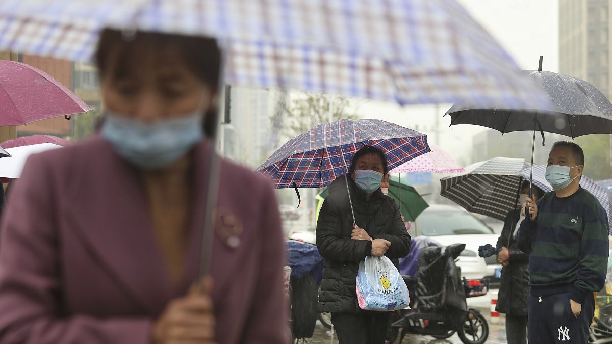 People wearing face masks to protect against COVID-19 wait in the rain to pick up children from a school in Wuhan.