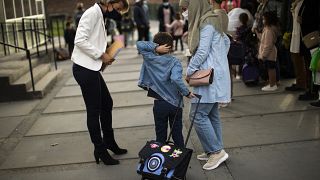 Criança e  a mãe são recebidas pela diretora da escola primária durante o primeiro dia de aula em Bruxelas.