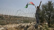 İsrail'in dikenli tellerle çevirdiği Naalin köyünde elinde Filistin bayrağı ile protesto yapan bir eylemci (arşiv)