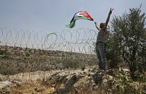 İsrail'in dikenli tellerle çevirdiği Naalin köyünde elinde Filistin bayrağı ile protesto yapan bir eylemci (arşiv)