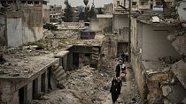 Suriye'nin İdlib kentinde hava bombardımanları sonucu yıkılan evlerin arasında yürüyen vatandaşlar