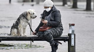 A woman with a face mask and a dog sit on a bench at the almost abandoned downtown in Duisburg, Germany, Monday, Jan. 25, 2021. 