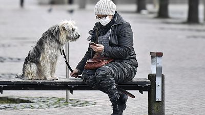 A woman with a face mask and a dog sit on a bench at the almost abandoned downtown in Duisburg, Germany, Monday, Jan. 25, 2021. 