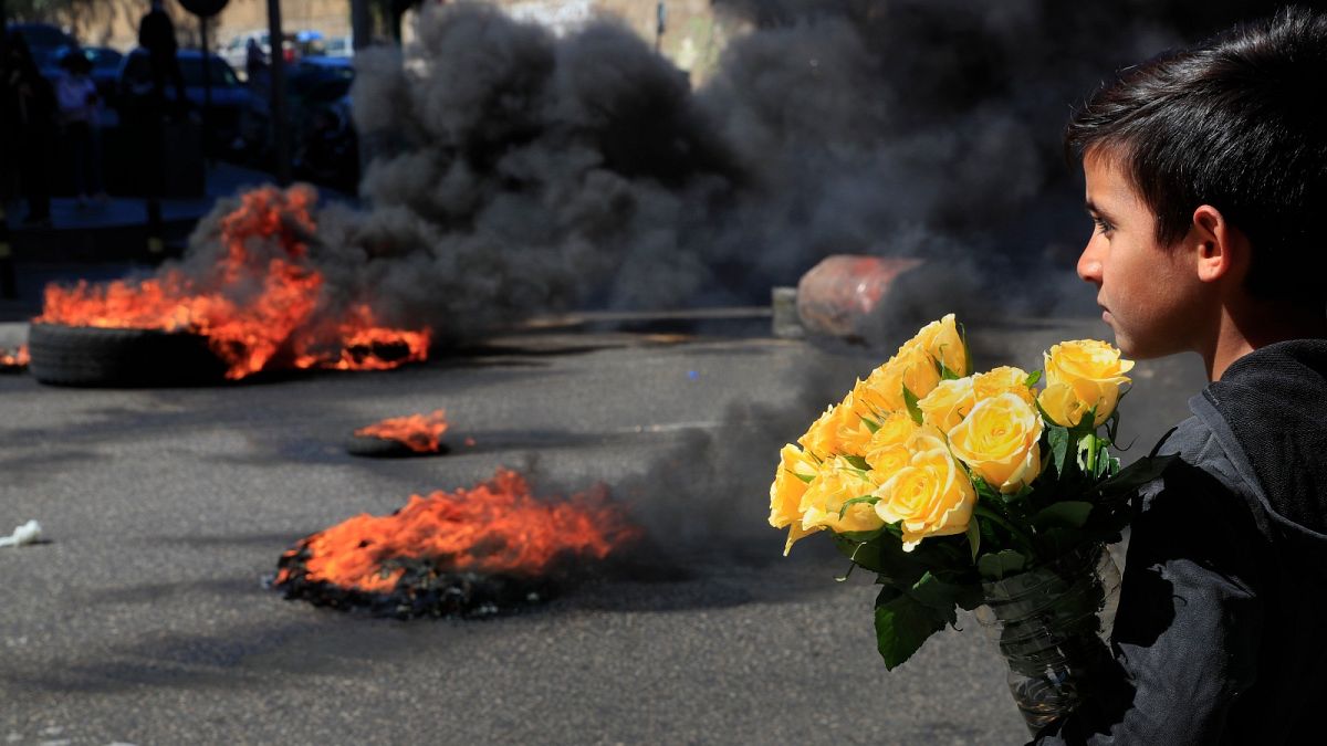 A Syrian boy who sells flowers on the street watches protesters burn tyres to block a main road during a demonstration in Beirut