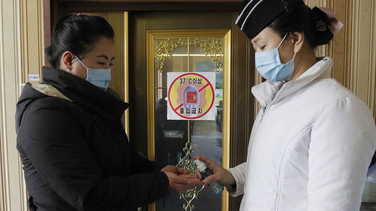 A staff member, right, of the Pongnam Noodle House disinfects the hands of a woman coming into its restaurant in Pyongyang, North Korea.