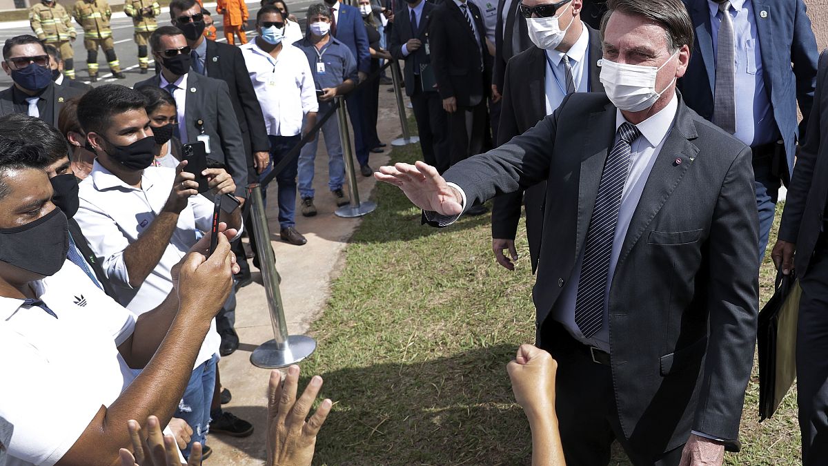 Wearing a mask, Brazil's President Jair Bolsonaro greets people in a neighborhood of Brasilia, Monday, Apr. 5, 2021. 