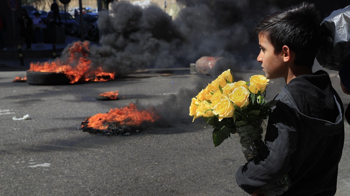 Un bambino siriano guarda i manifestanti che bruciano pneumatici per bloccare una strada principale durante una manifestazione a Beirut 