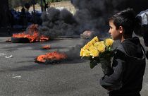 Un bambino siriano guarda i manifestanti che bruciano pneumatici per bloccare una strada principale durante una manifestazione a Beirut