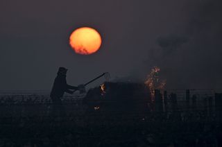 A winegrower burns a bale of straw in the vineyards to protect them from frost on April 7, 2021 as the sun rises at the heart of the Vouvray vineyard in Touraine, France