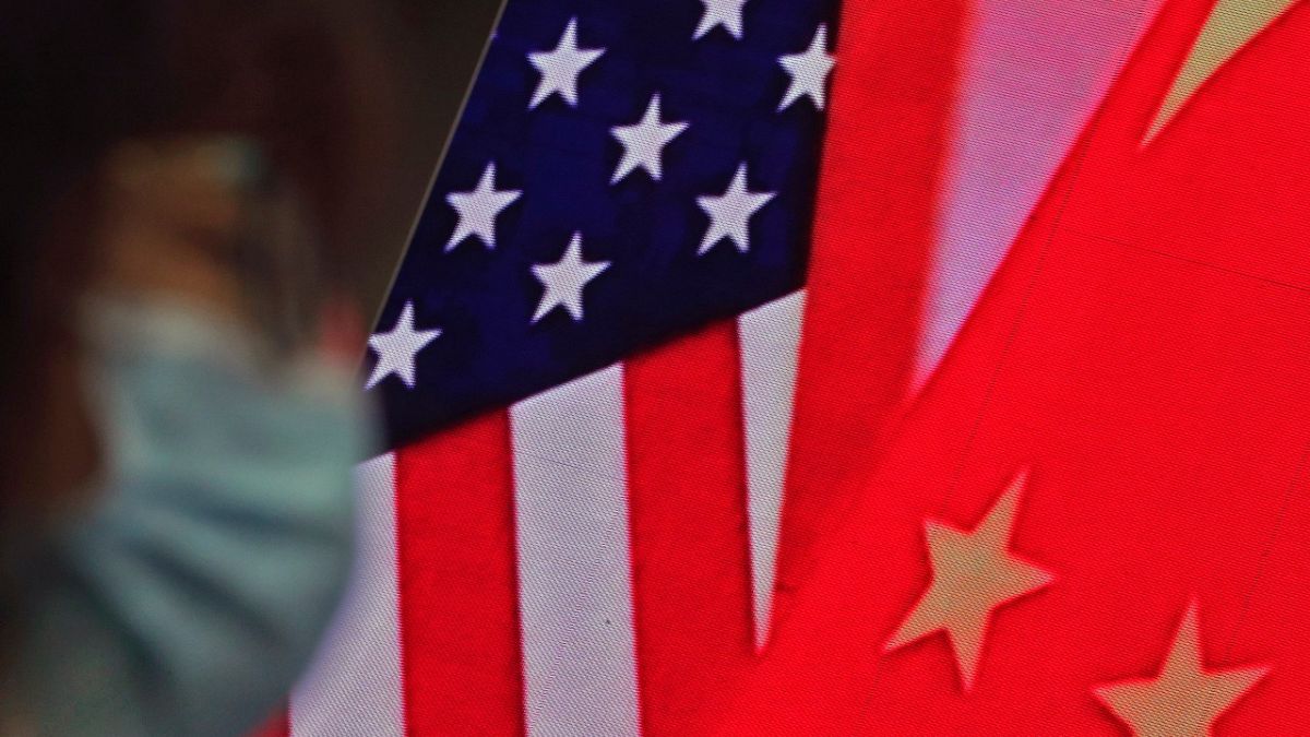 امراة تمشي حذو شاشة يظهر عليها العلمان الأمريكي والصيني بينما تستمع إلى خطاب وزير الخارجية الصيني. 2021/02/22