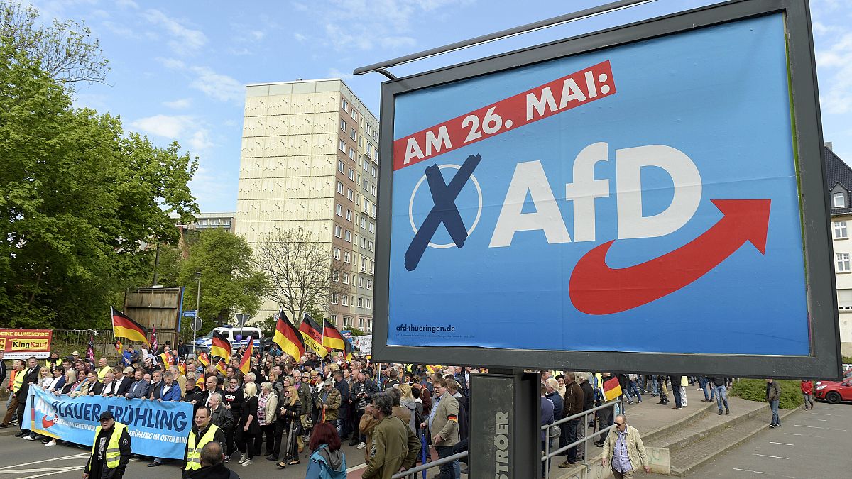 This picture taken May 1, 2019 shows AfD supporters walkin along a party elections poster in Erfurt, Germany. 