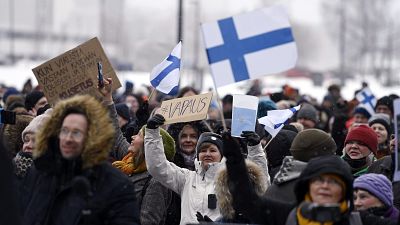 A group of people hold placards during a protest against the Finnish government's regulations to fight the coronavirus pandemic in Helsinki, March 20, 2021.