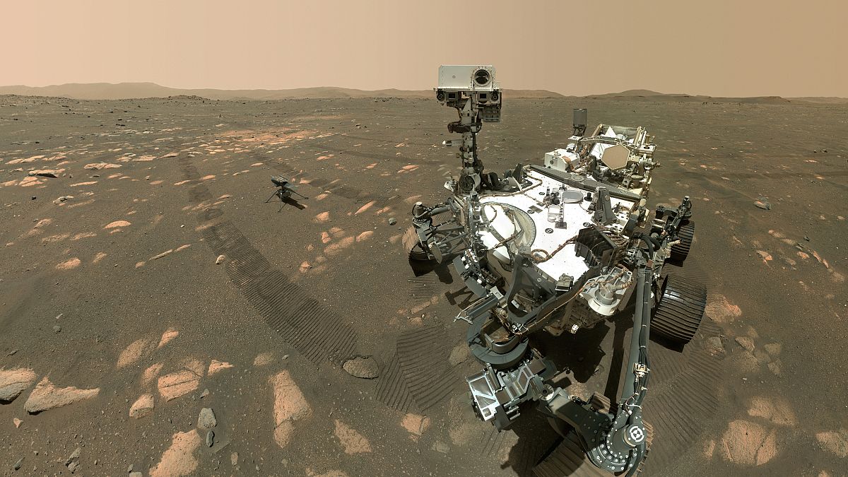 A selfie by the Perseverance Mars rover with the Ingenuity helicopter a few metres behind it.