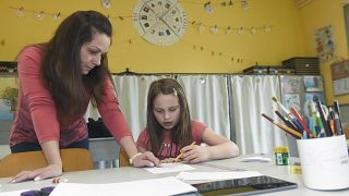 A teaching assistant helps a child with her assigment in a school in Budapest, Hungary Tuesday, March 31, 2020.