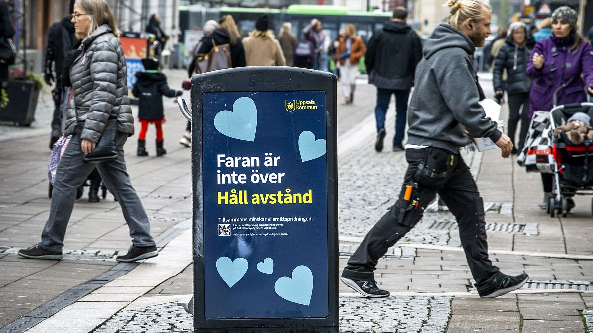People walk past a bin with a sign reading "The danger is not over. Keep your distance" in a pedestrian street in central Uppsala, Sweden. October 21, 2020.