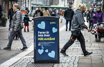 People walk past a bin with a sign reading "The danger is not over. Keep your distance" in a pedestrian street in central Uppsala, Sweden. October 21, 2020.