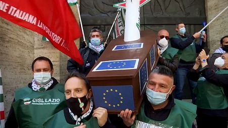 Workers of Alitalia carrying a coffin with a plane inside