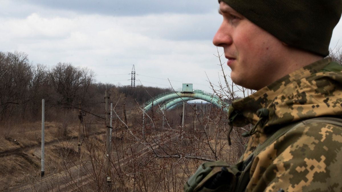 A Ukrainian soldier looks towards the frontline.  The pipes behind him carry water from an area controlled by Kyiv to the area controlled by the Russian-backed separatists