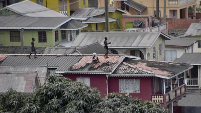 Varias personas limpian la ceniza volcánica del tejado de una casa tras la erupción del volcán La Soufriere, en San Vicente