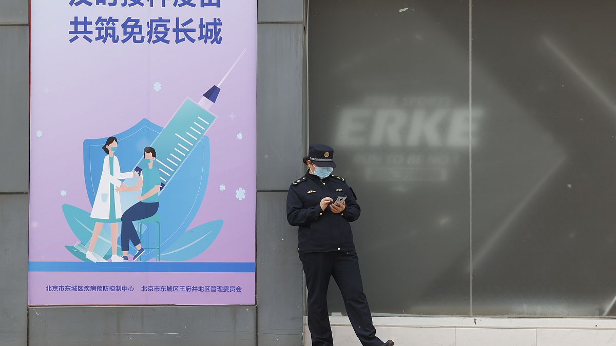 A worker stands outside a vaccination site with a sign saying "Timely vaccination to build the Great Wall of Immunity together" in Beijing. April 9, 2021.