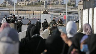 قوات الأمن الإسرائيلية يحرسون حاجز قلنديا بالقرب من بلدة رام الله بالضفة الغربية، بينما تنتظر فلسطينيات لدخول القدس لحضور صلاة الجمعة الأولى لشهر رمضان في المسجد الأقصى