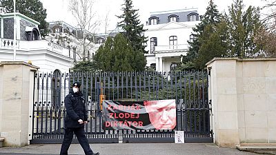 A policeman walks by a poster attached by protesters to a gate of the Russian embassy in Prague, Czech Republic, on Friday