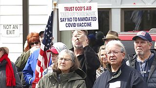 A sign denouncing the COVID-19 vaccine is held up in the crowd gathered at a protest