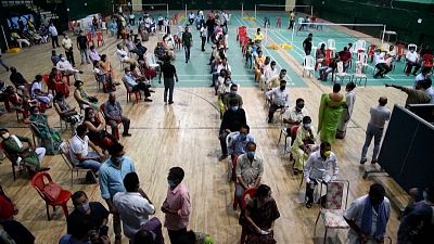 People wait to take doses of the Covaxin coronavirus vaccine at an indoor stadium.