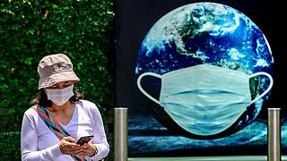 A woman walks in front of a poster showing earth wearing a protective facemask