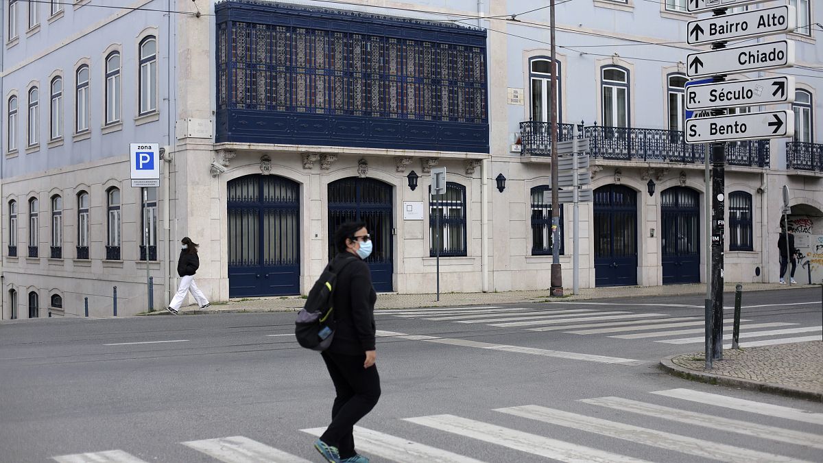 People wearing face masks walk across a street in Lisbon, Wednesday, Feb. 17, 2021. 