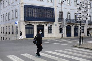 People wearing face masks walk across a street in Lisbon, Wednesday, Feb. 17, 2021.