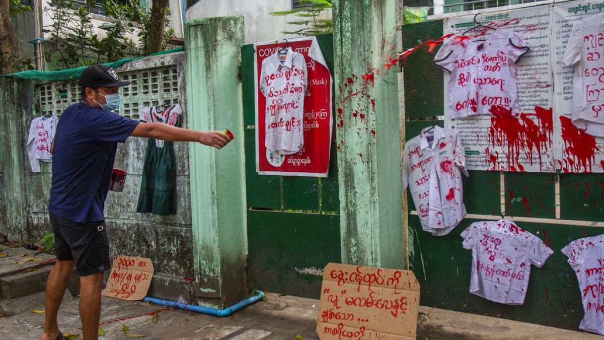 An anti-coup protester splashes red paint on student uniforms after they hanged them outside a school during a demonstration against the re-opening of the school by the junta 
