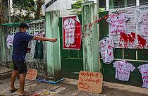 An anti-coup protester splashes red paint on student uniforms after they hanged them outside a school during a demonstration against the re-opening of the school by the junta