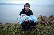Ege Denizi'ni sandalla geçtikten sonra Yunanistan'ın Midilli adasına bağlı Skala Sikaminias köyüne yürürken kucağındaki bebekle yol kenarında dinlenen bir göçmen