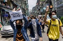 A protester holds a sign in support of the National Unity Government (NUG) as others make the three-finger salute during a demonstration against the military coup