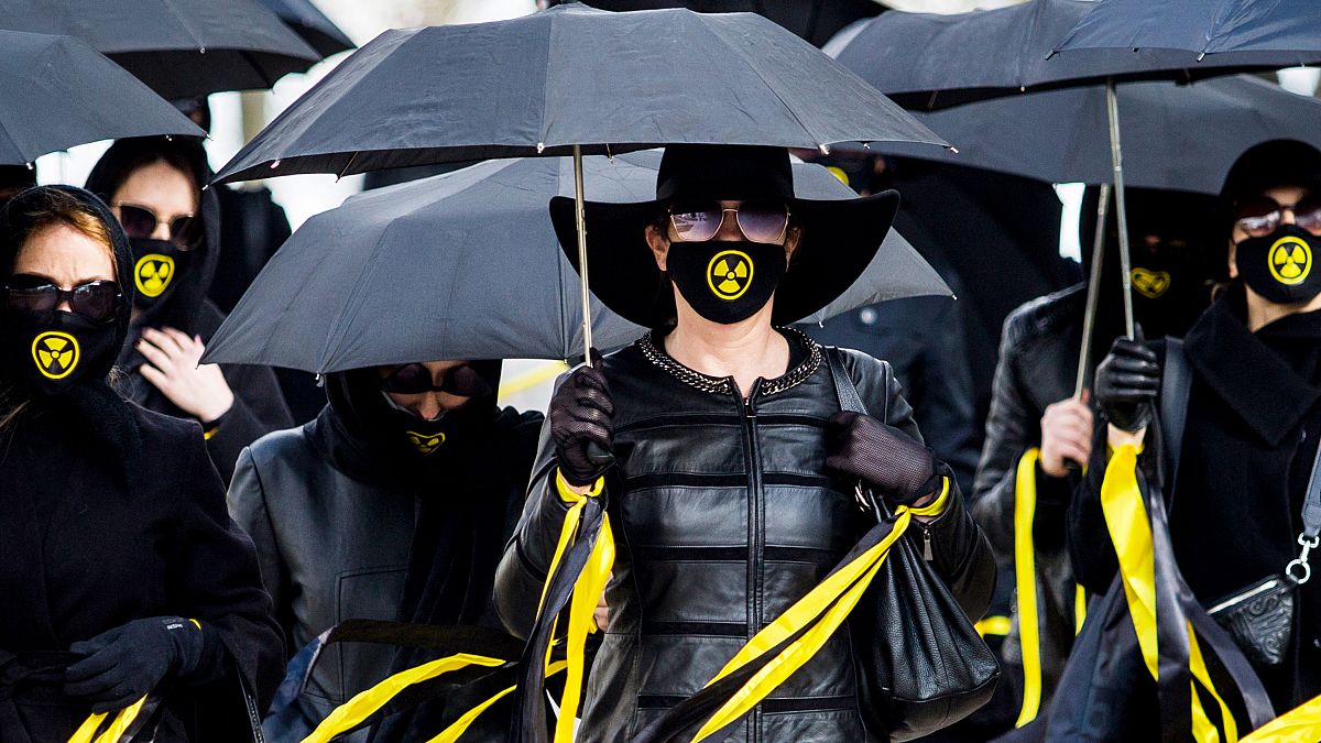 Women wearing black clothing and face masks with radioactivity sign march under umbrellas in Minsk. April 26, 2021