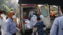 Profissionais de saúde transferem corpos de uma ambulância para um crematório em Nova Deli
