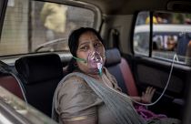 A COVID-19 patient sits inside a car and breathes with the help of oxygen