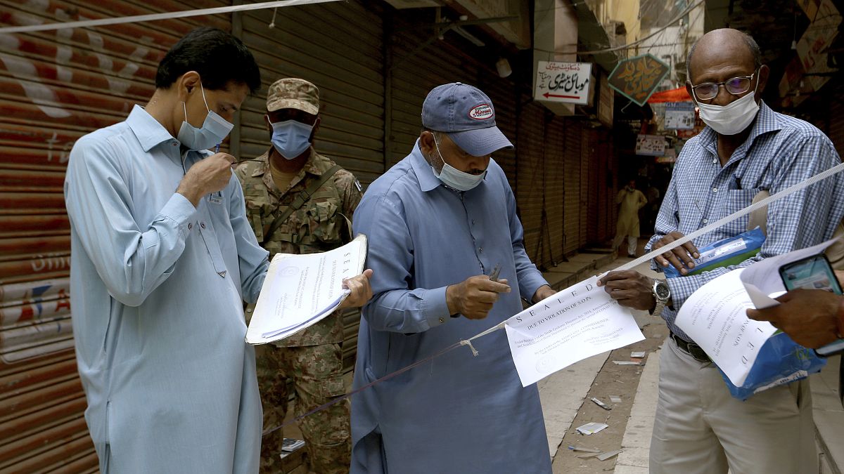 Officials gather to seal a market on the violation of new restrictions announced by government to control the spread of the coronavirus, in Karachi, Pakistan, Saturday.