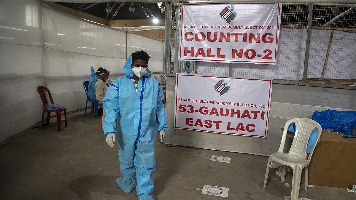A counting agent in protective suit walks past officials during the counting of votes of Assam state assembly election in Gauhati, India, Sunday, May 2, 2021. 