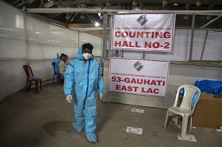 A counting agent in protective suit walks past officials during the counting of votes of Assam state assembly election in Gauhati, India, Sunday, May 2, 2021.