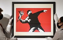 Gallery technicians display a Banksy artwork called "Love is in the Air" read for auction.