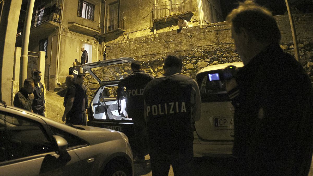 ضباط وعناصر الشرطة يقفون خارج منزل المشتبه به أثناء عملية في سينوبولي، جنوب إيطاليا.