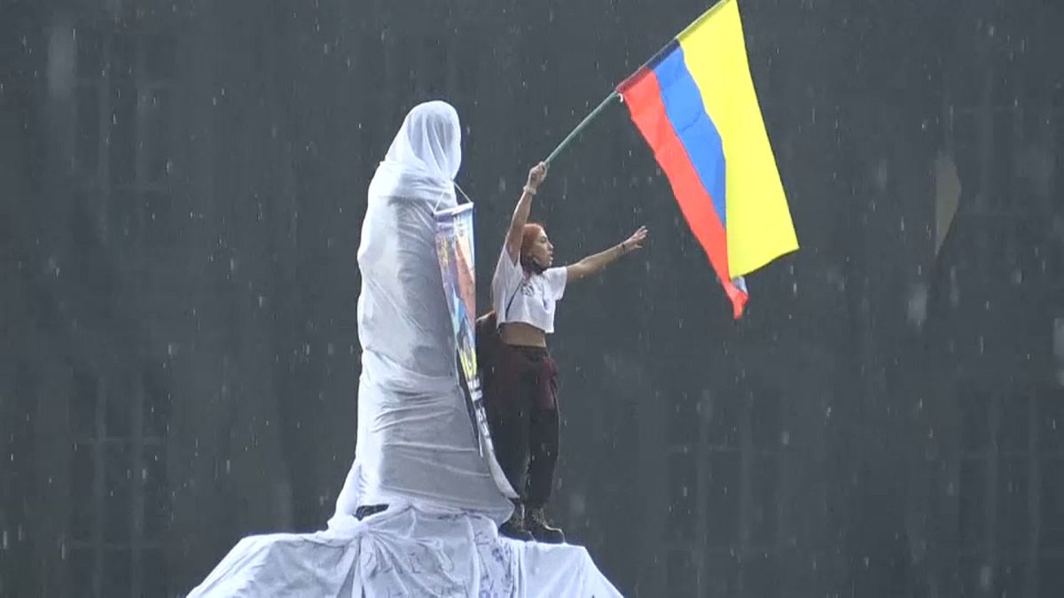 Un chica ondea una bandera de colombia subida en una estatua en el inicio del paro nacional de este miércoles 5 de mayo de 2021