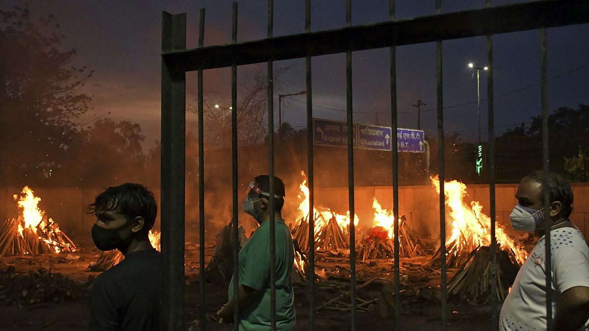 People watch burning funeral pyres of their relatives who died of COVID-19 in a ground that has been converted into a crematorium in New Delhi, India, Thursday, May 6, 2021.