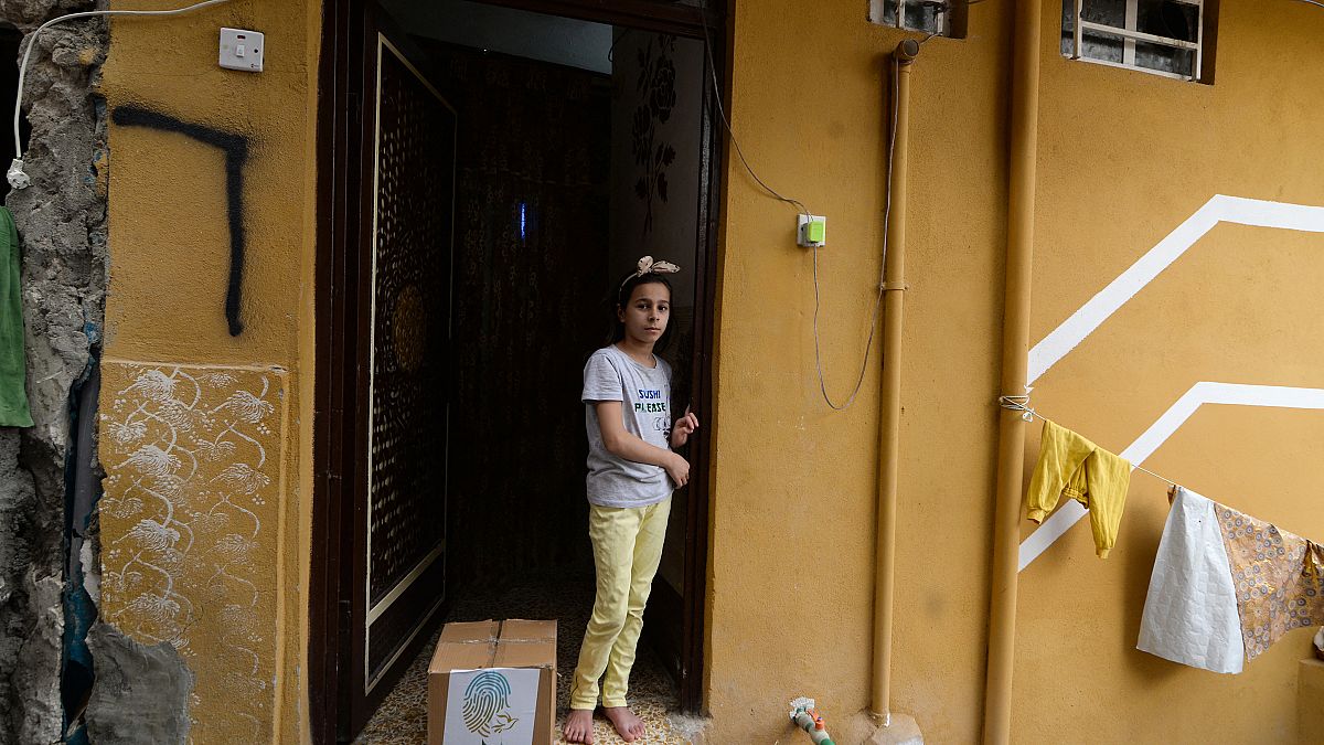طفلة عراقية تقف على عتبة منزل ذويها وإلى جانبها سلة مساعدات غذائية تقدمة الجمعيات الخيرية في مدينة الموصل شمال البلاد خلال شهر رمضان المبارك